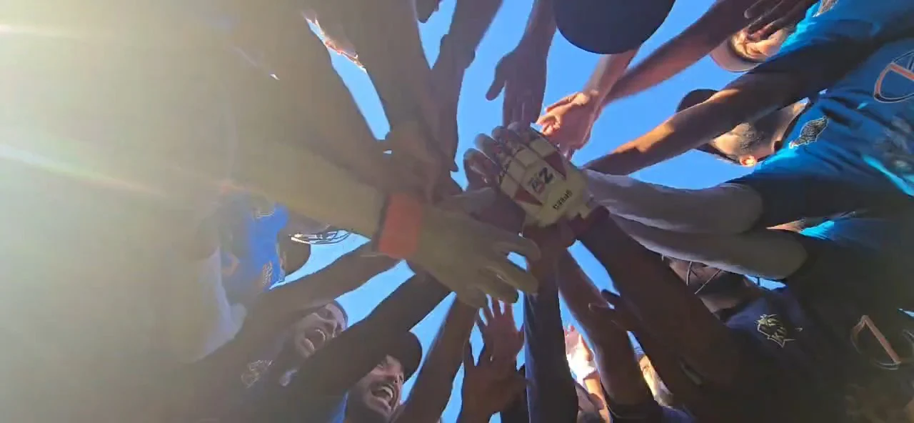 Cricket players joining hands in a team huddle